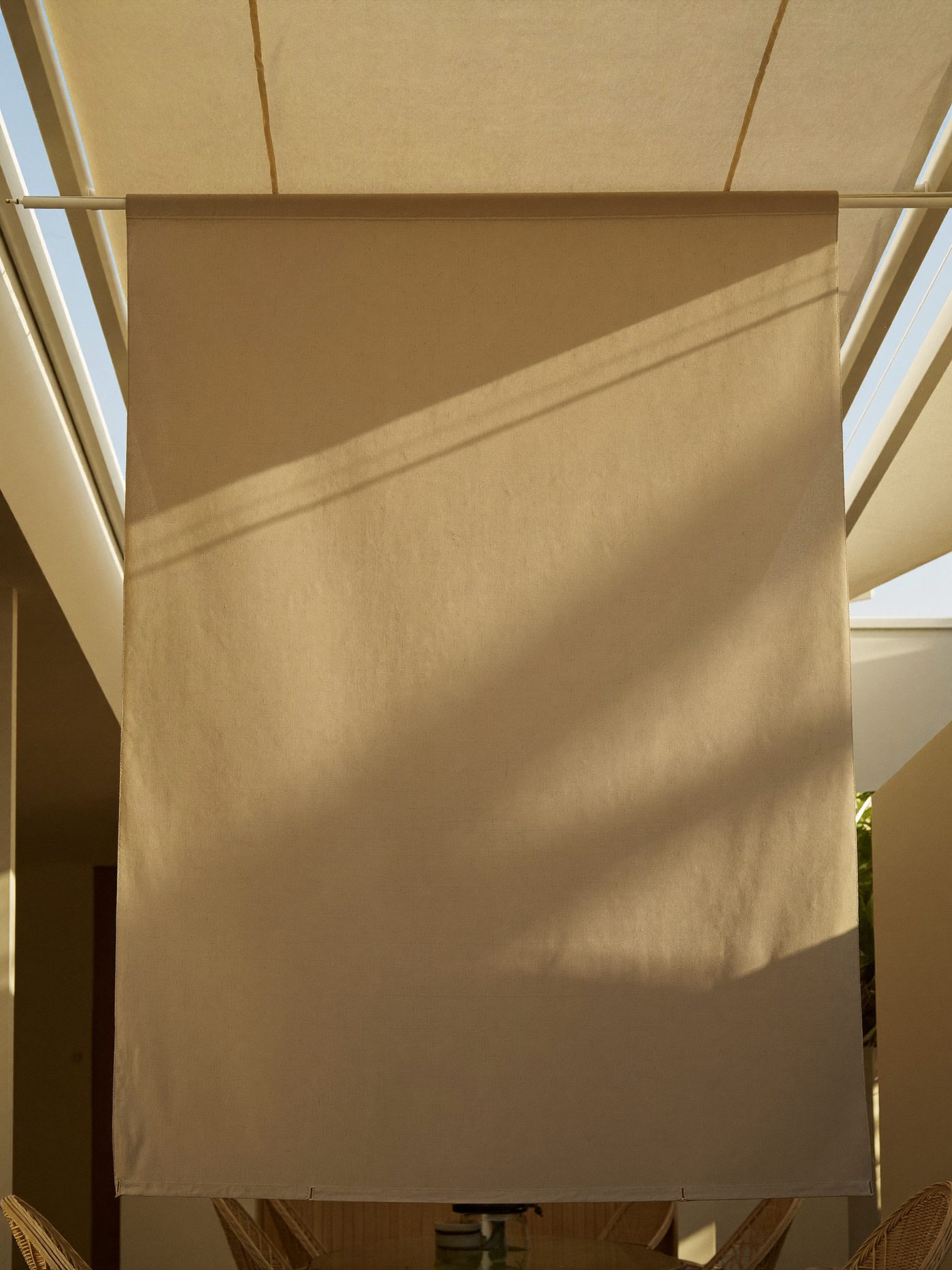 Pérgola com toldo de lona estendido sobre móveis de vime no quintal