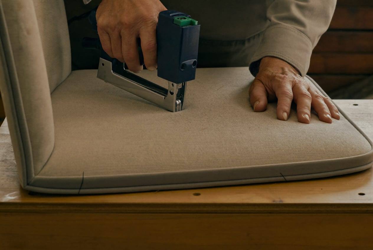 Mãos grampeando tecido na parte de baixo do assento de uma cadeira